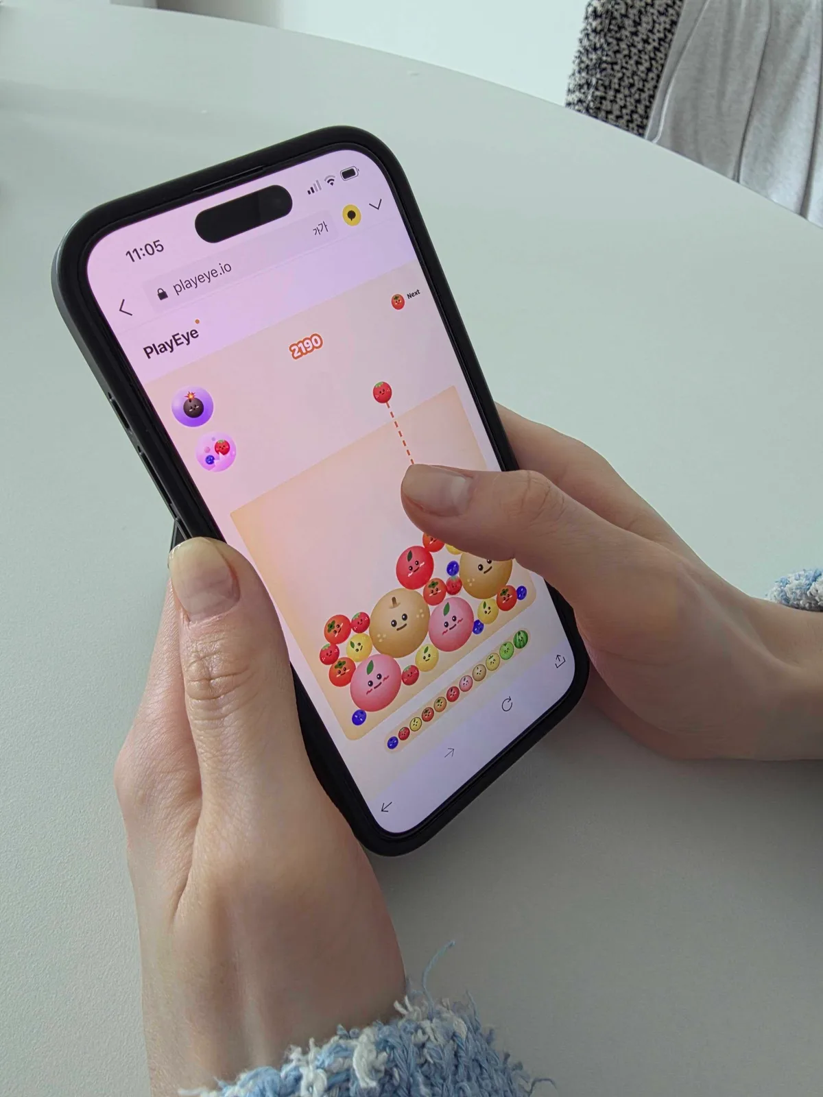 Two hands holding an iPhone showing Watermelon Game at 2,190 points, with a pear and a peach resting low in the center of the board